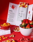 Assorted snacks including strawberries, golden berries, and chocolate bars on a red surface with magno chocolates brand name