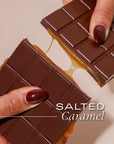 A chocolate bar with salted caramel filling held by hands against a beige background.