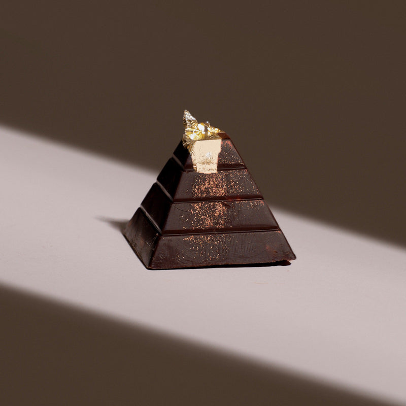 A luxury chocolate bonbon in the shape of a pyramid with a touch of 24K gold leaf