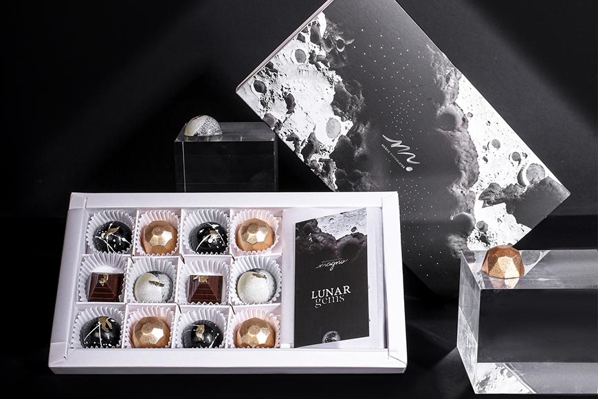 Gourmet chocolate gift boxes over a dark backdrop with a light above shining on the hand painted chocolates inside