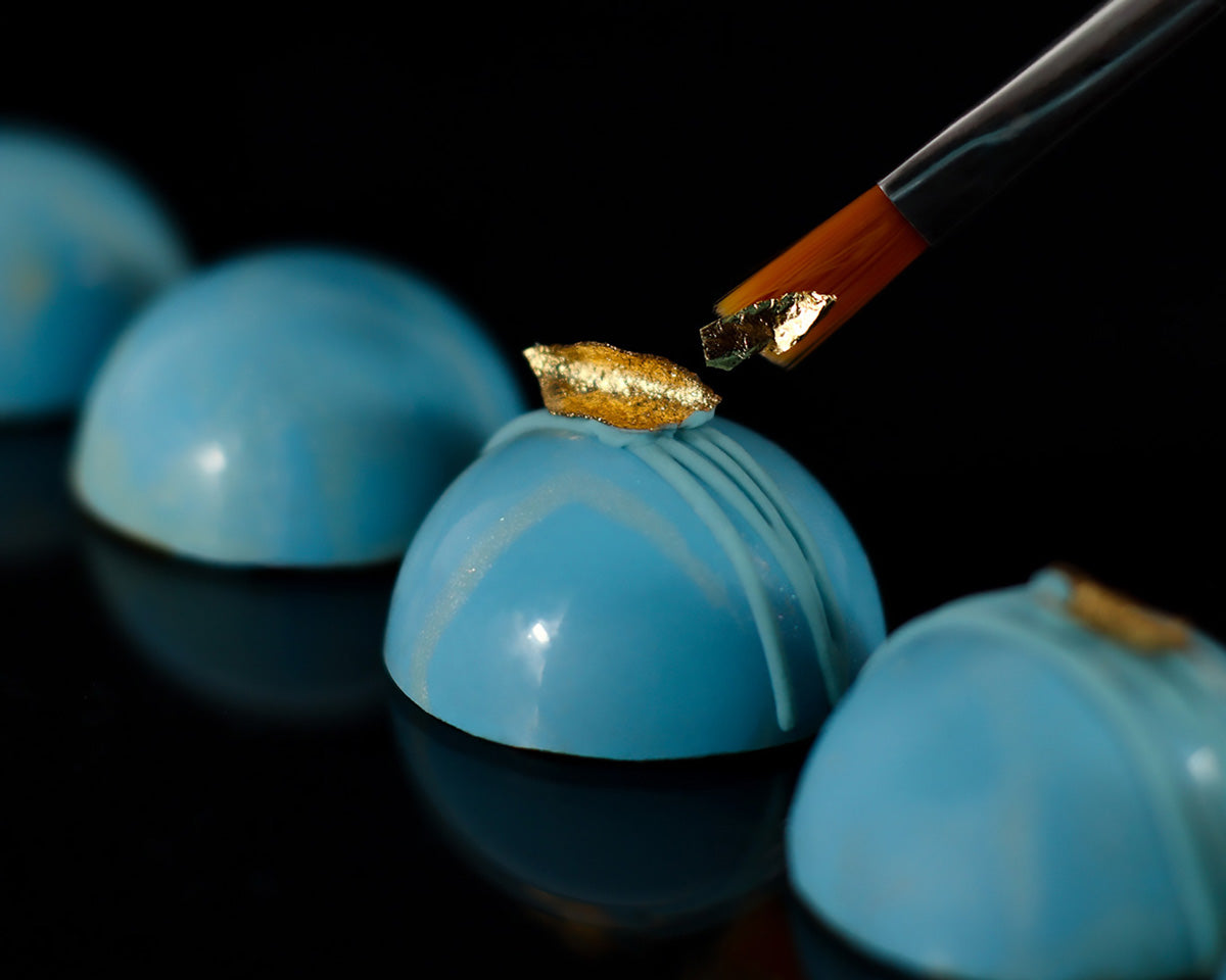 Paintbrush adding gold to the hand painted gourmet chocolate bonbons made with single origin Colombian Cacao