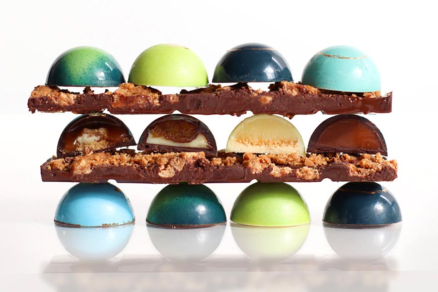 an assortment of shiny hand painted chocolates stacked on top of tasty looking chocolate bars