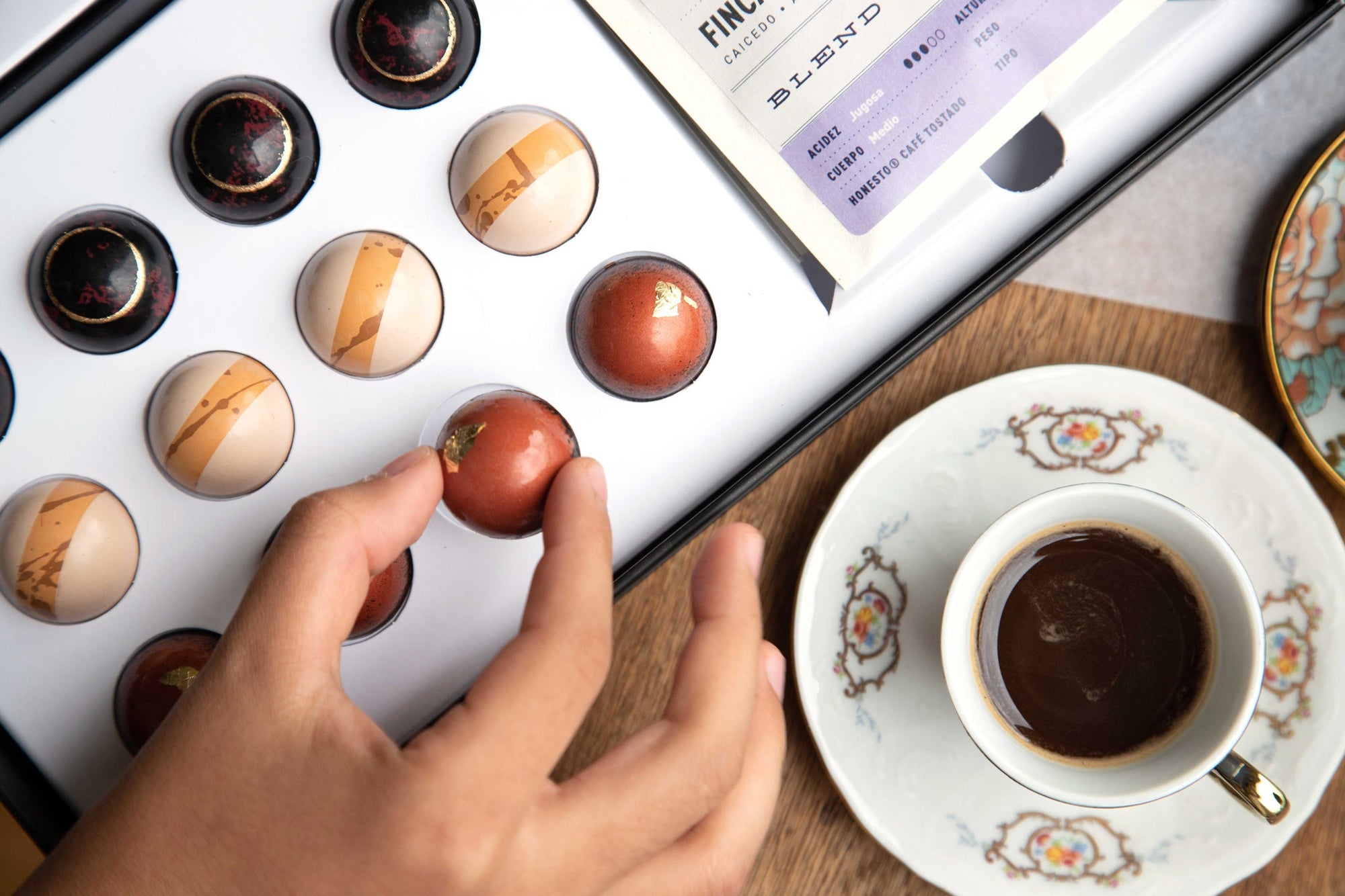 Close up of a hand picking up the gourmet chocolate bonbon next to a cup of Colombian Coffee