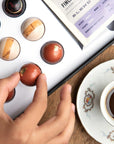 Close up of a hand picking up the gourmet chocolate bonbon next to a cup of Colombian Coffee